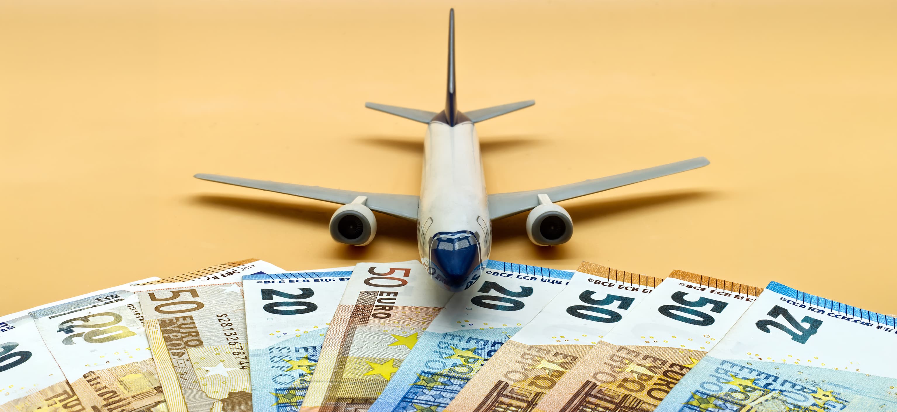 Toy airplane surrounded by fanned-out euro banknotes, representing the true cost of a flight