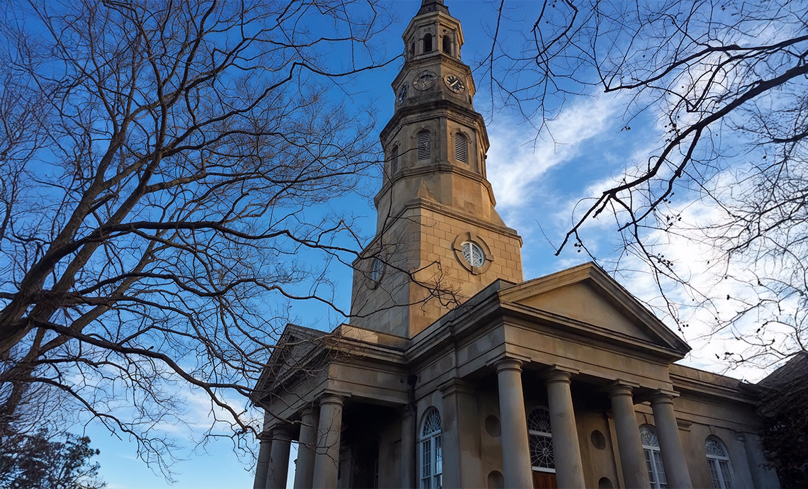 historic st philips cathedral exterior with tall clock tower steeple and neoclassical columns against a blue sky charleston sc